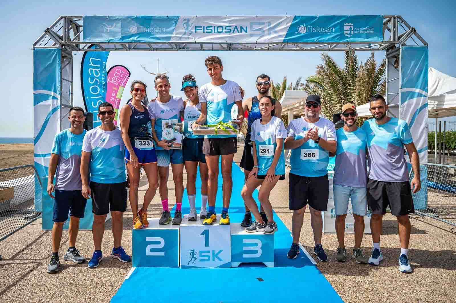 Podio de la Fisiosan 5K en Playa Honda, con los premiados y la organización bajo el arco de meta