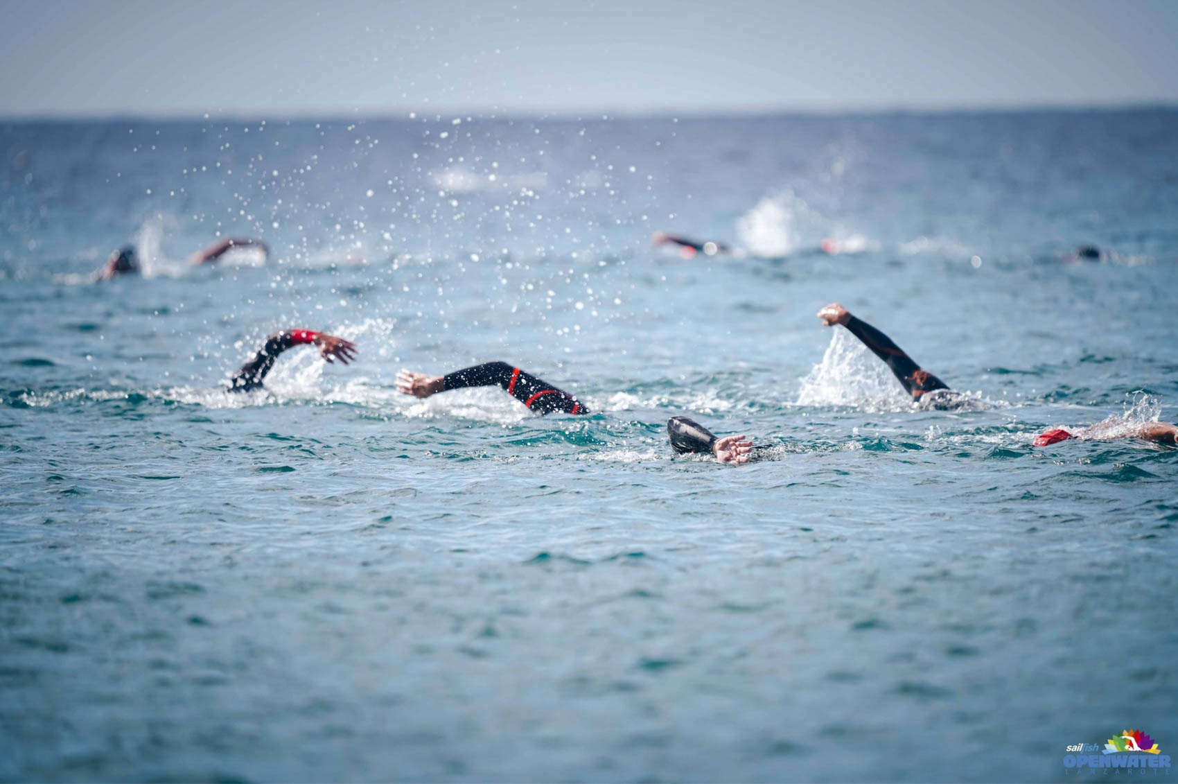 Several swimmers mid-crawl in open water, arms up and spray flying all around them